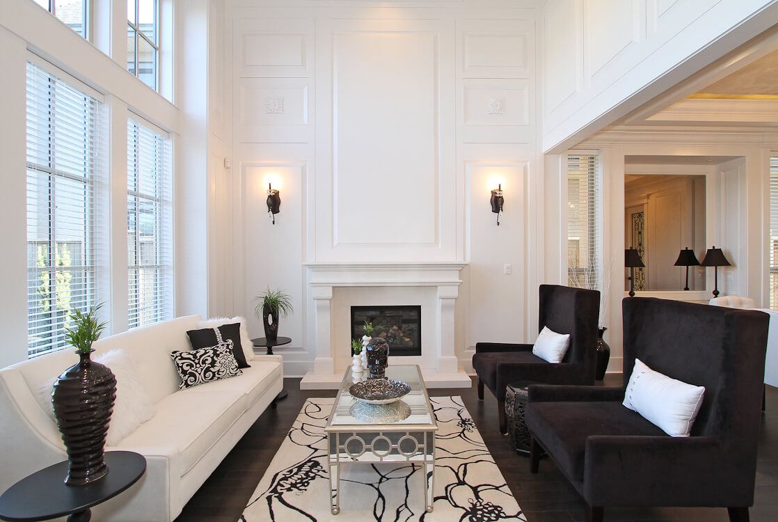 Lyon stone fireplace mantel in a grand white living room with tall windows and dark accent chairs