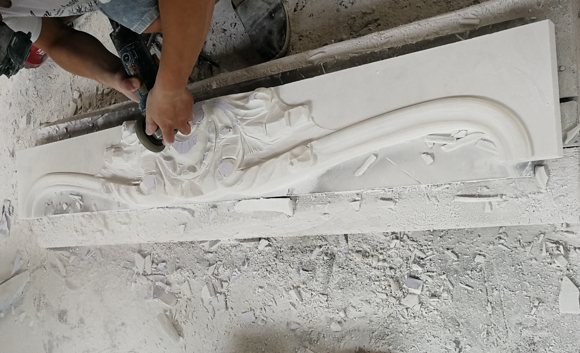 A stone carver hand-carving ornate details into a limestone mantel in the workshop