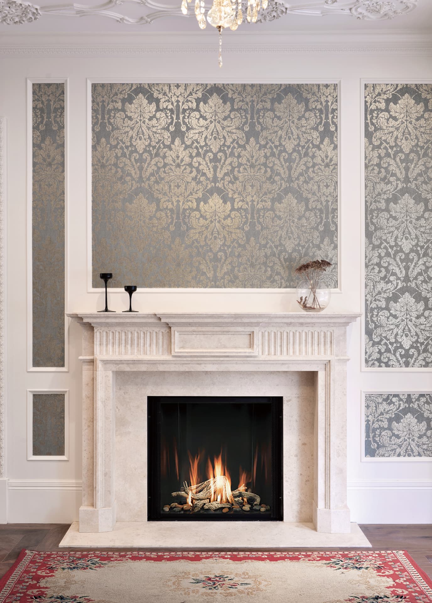 Octavia hand-carved stone fireplace mantel with a lit fire in an elegant paneled room